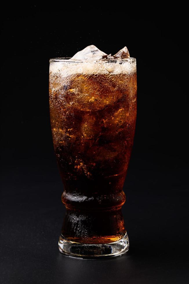 cola in glas met heldere ijsblokjes geïsoleerd op zwarte achtergrond foto