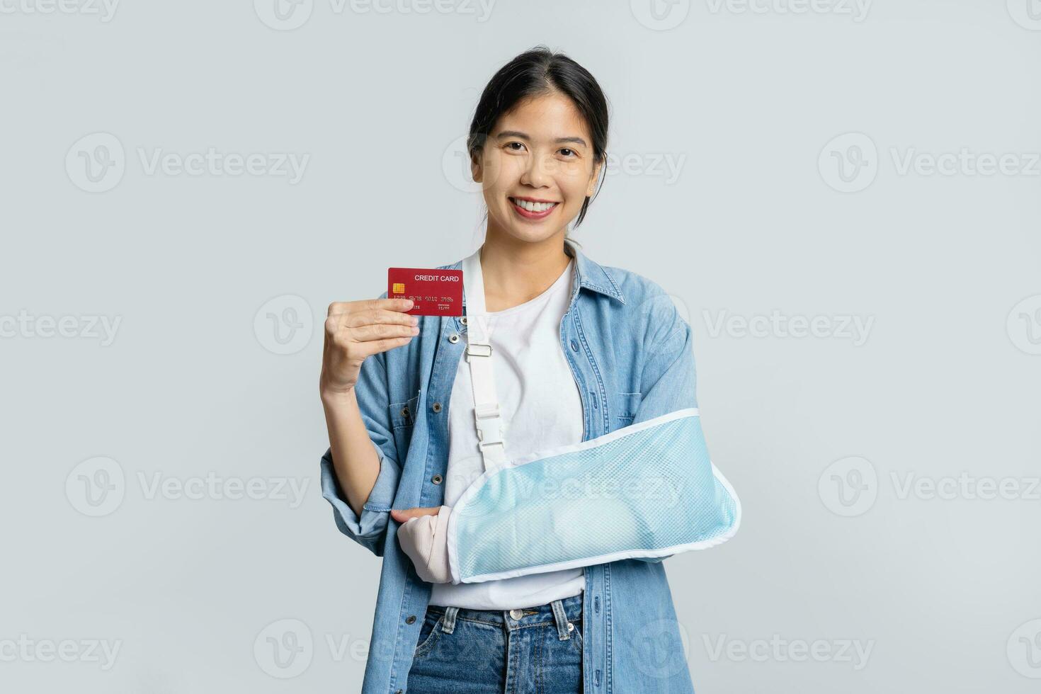 jong mooi Aziatisch kantoor arbeider in gips ten gevolge naar gebroken arm in ongeluk terwijl Holding credit kaart geïsoleerd Aan wit achtergrond. ongeluk verzekering of medisch onkosten concept. foto