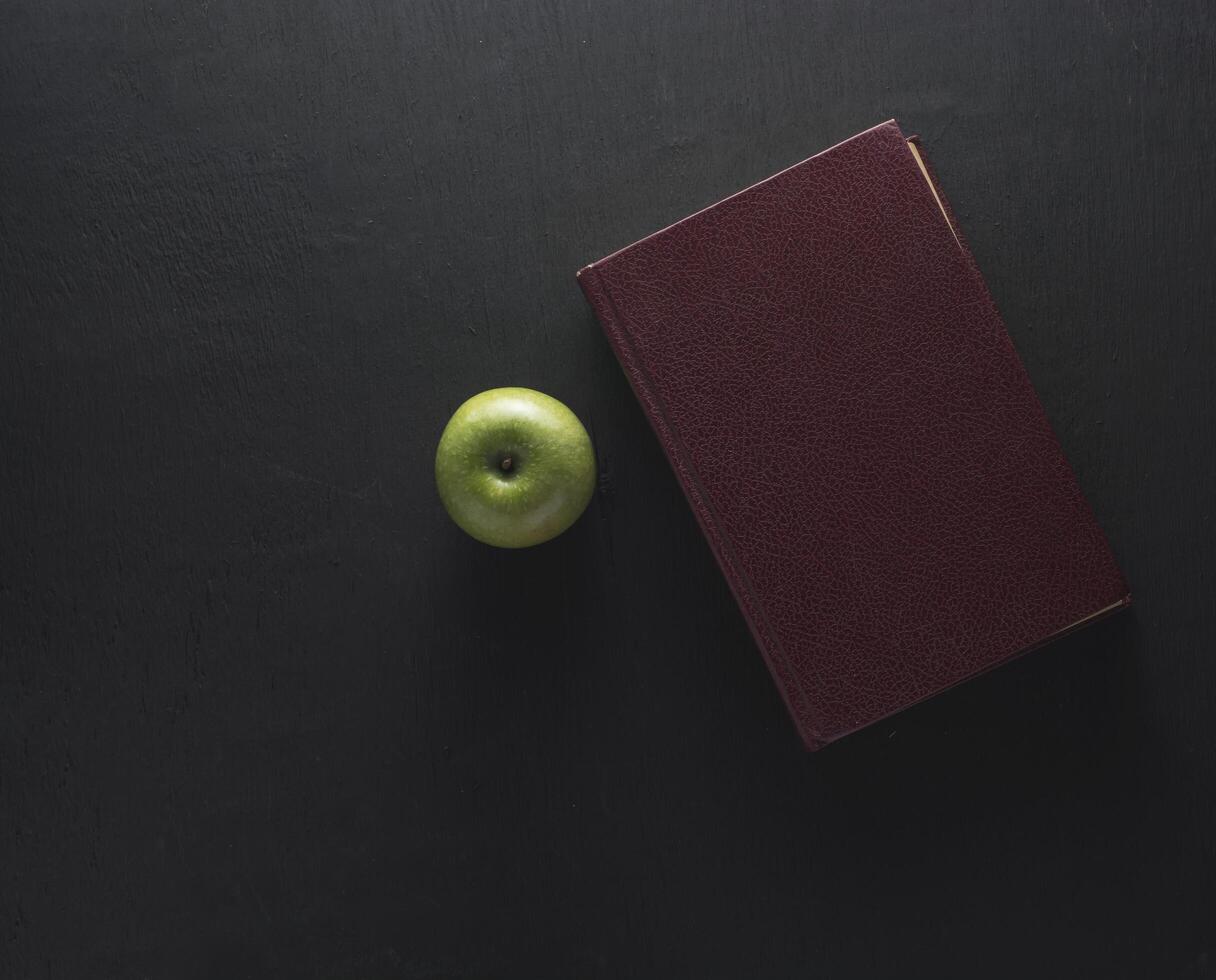 bovenaanzicht van groene appel met oud boek op zwarte houten achtergrond foto