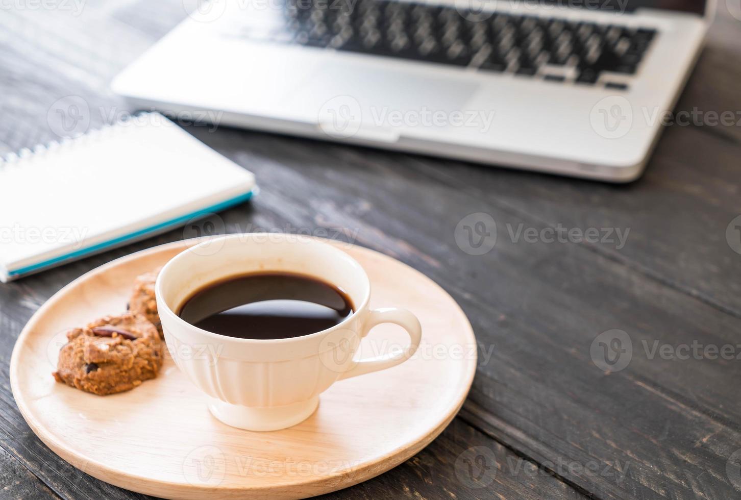 zwarte koffie en koekjes met laptop en notebook op tafel foto