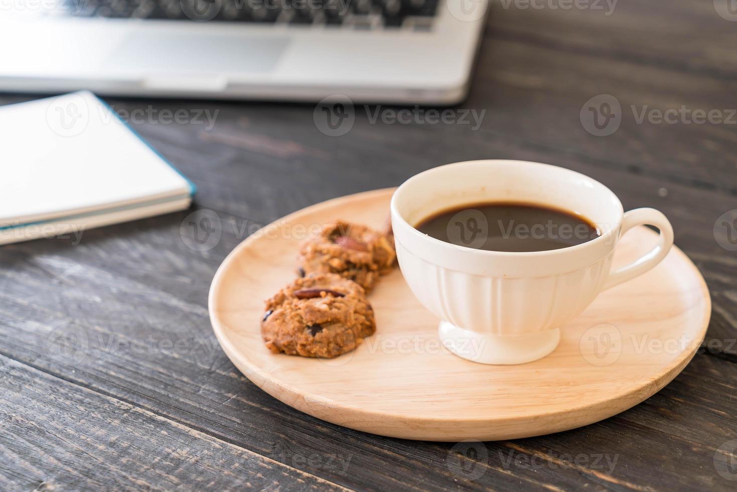 zwarte koffie en koekjes met laptop en notebook op tafel foto