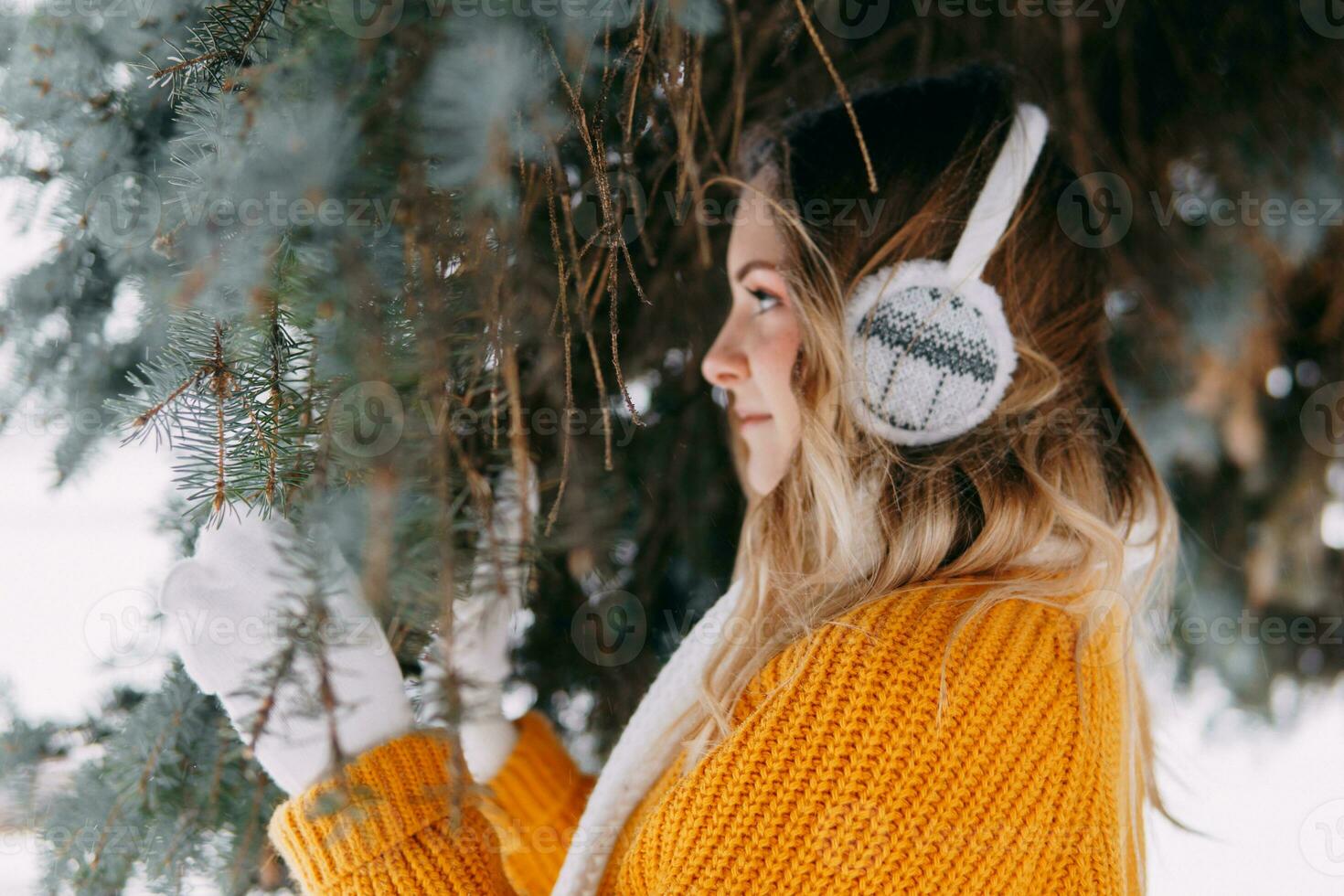 tiener blond in een geel trui buiten in winter. een tiener- meisje Aan een wandelen in winter kleren in een besneeuwd Woud foto