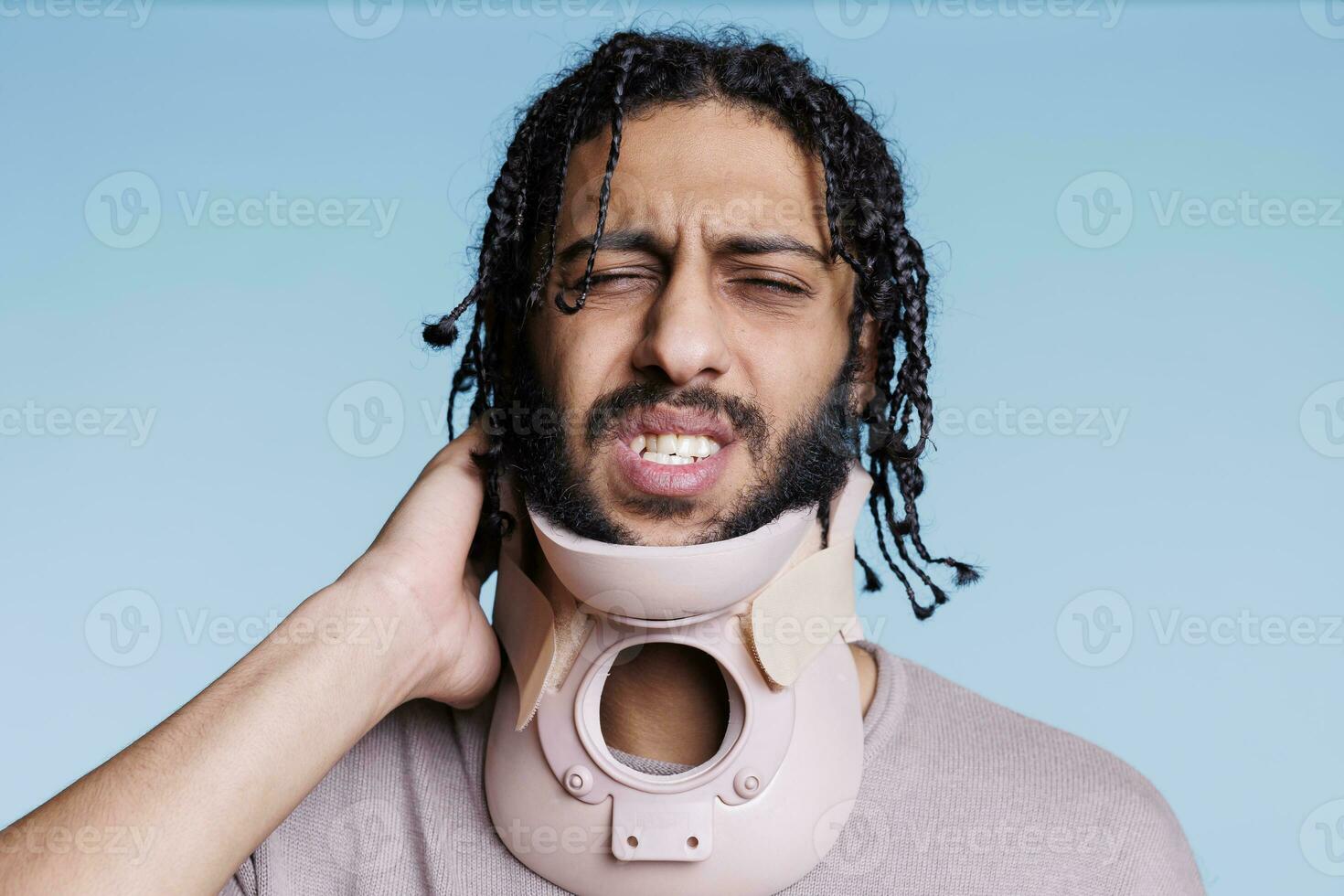 Arabisch Mens vervelend cervicaal halsband en grimassen in pijn terwijl aanraken nek. gewond jong persoon met pijnlijk gelaats uitdrukking vervelend beugel, herstellen van spinal trauma foto