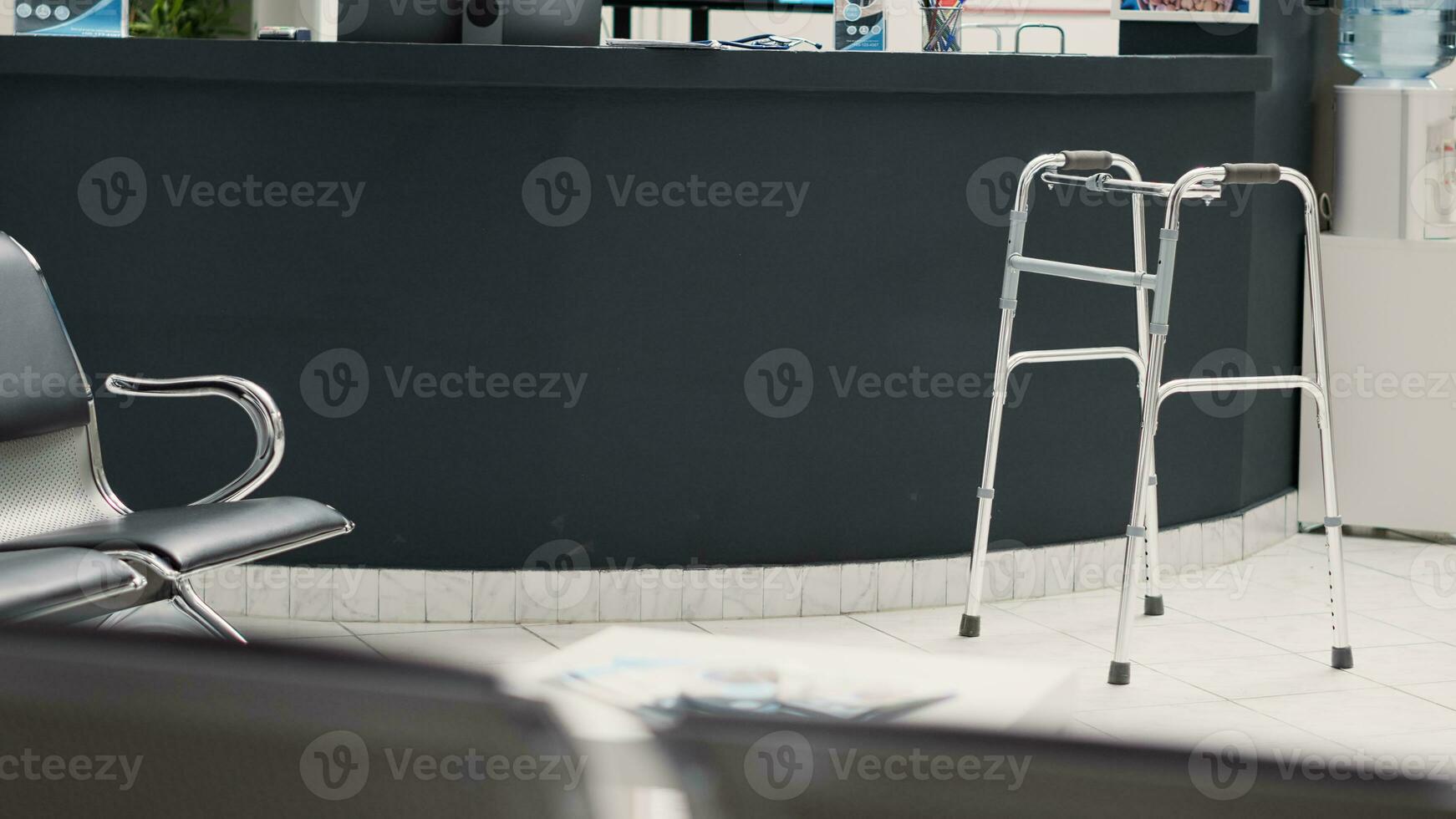 klinisch aan het wachten Oppervlakte met wandelen kader in lobby, leeg ontvangst voorkant bureau met medisch rapporten en stoelen in aan het wachten kamer. ziekenhuis gang met steun naar helpen met fysiek beperking. foto