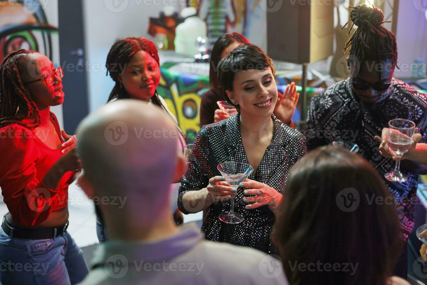 glimlachen vrouw drinken alcohol met groep van vrienden en genieten van disco partij in nachtclub. vrolijk jong mensen Holding drank bril, gezegde geroosterd brood en naar een discotheek gaan Aan dansvloer foto