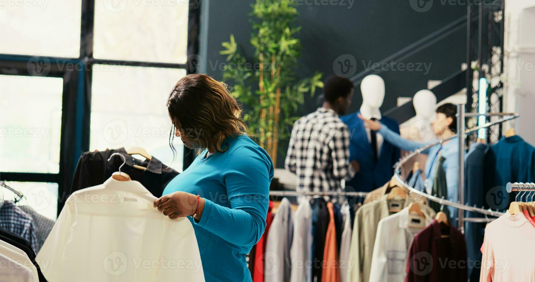 Afrikaanse Amerikaans klant op zoek Bij nieuw mode verzameling, boodschappen doen voor modieus kleren in modern boetiek. elegant cliënt controle rekken met modieus handelswaar, analyseren kleding stof in op te slaan foto