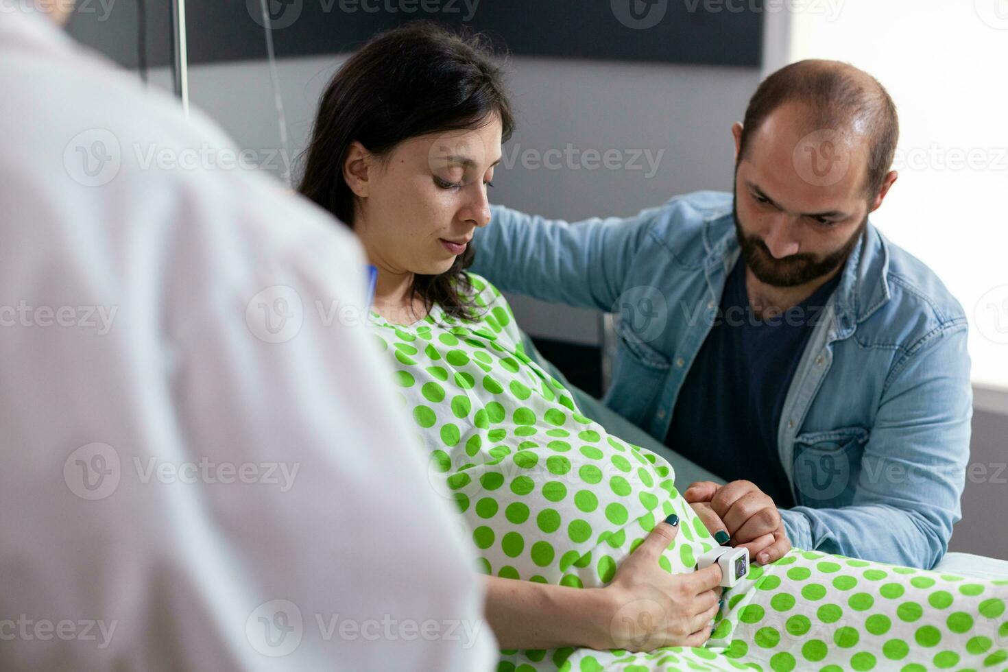 gynaecoloog controle zwanger vrouw symptomen voordat medisch chirurgie, bespreken bevalling werkwijze met toekomst ouders in ziekenhuis afdeling. geduldig met zwangerschap aan het liegen in bed in moederschap kliniek foto