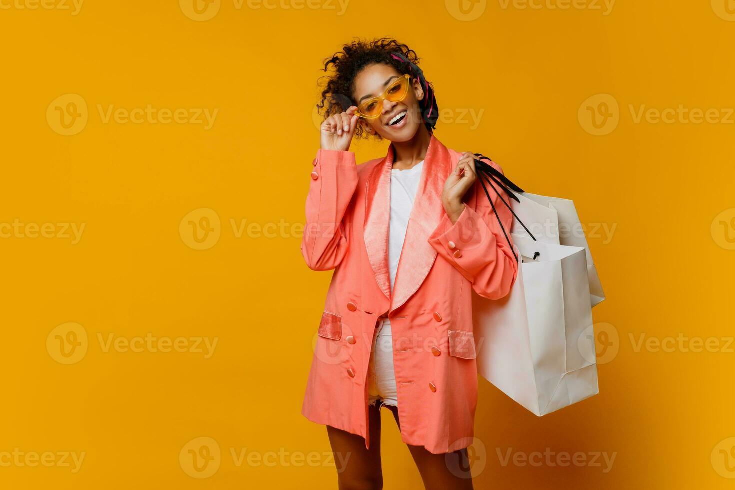 modieus positief vrouw met donker huid Holding boodschappen doen Tassen, staand Aan geel achtergrond .trendy voorjaar modieus Look. foto