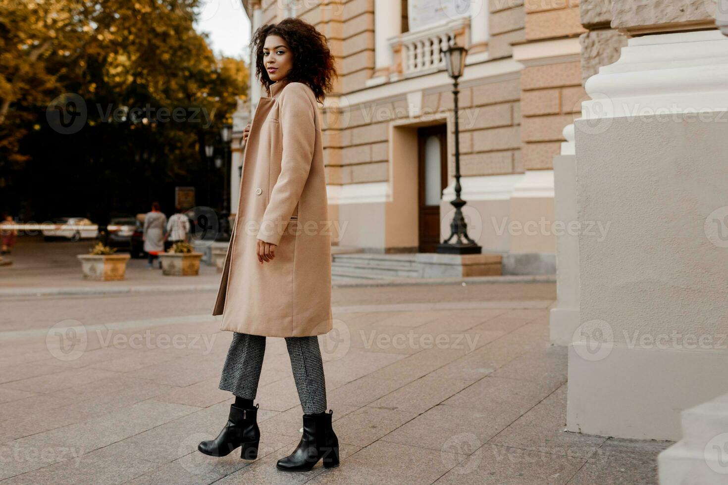 mode vol lengte beeld van elegant zwart vrouw in elegant luxe beige jas en fluweel trui, hoogte hakken, wandelen buitenshuis. foto