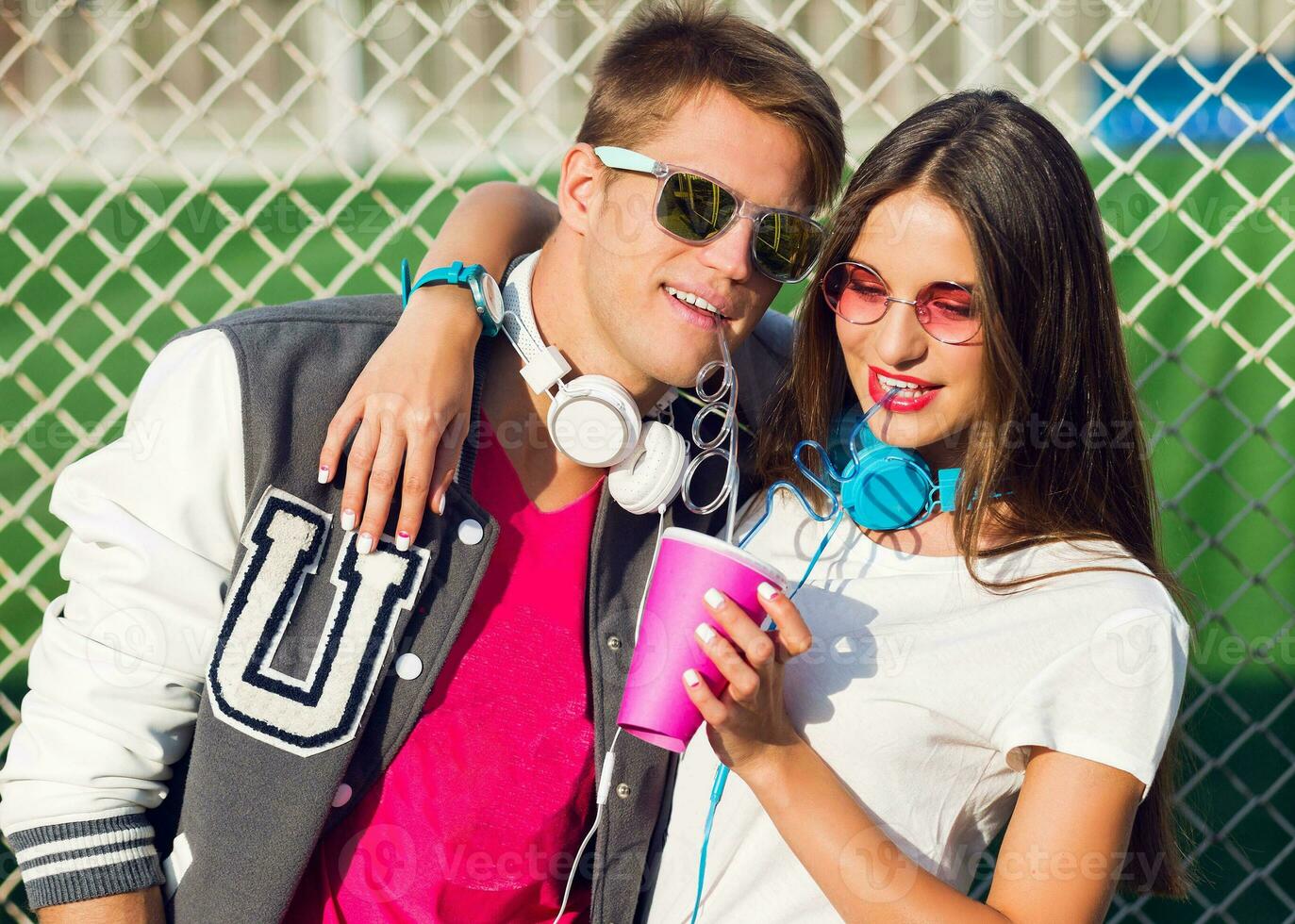 helder zomer portret van een mooi jong paar Aan een zonnig dag, hipsters, verbazingwekkend meisje met rood lippen, vervelend zonnebril en aantrekkelijk knap vent met een denim jasje genieten van sap. foto