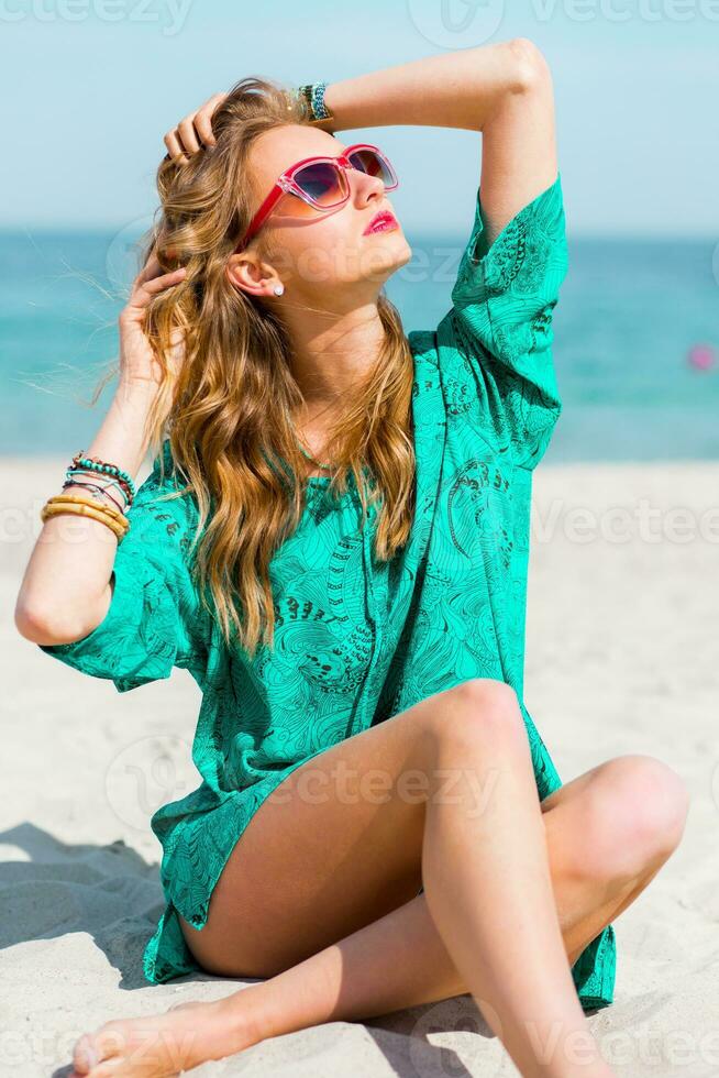 buitenshuis zomer portret van mooi jong blond mooi vrouw in koel zonnebril poseren Aan de zonnig tropisch strand. vervelend elegant strand kleding. foto