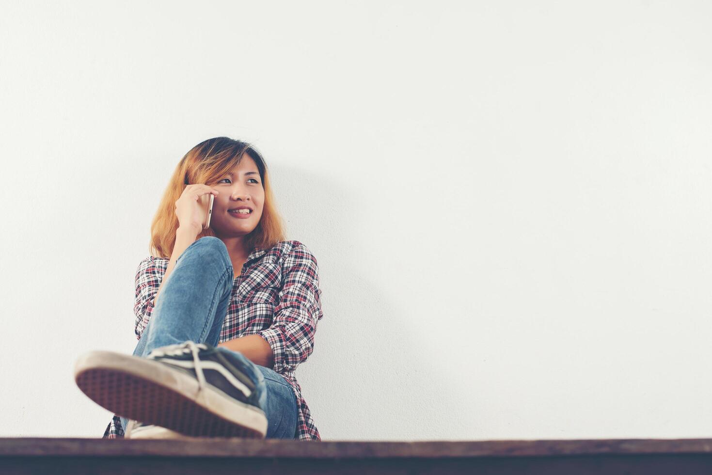 gelukkige hipster vrouw zittend op houten vloer praten met telefoon foto