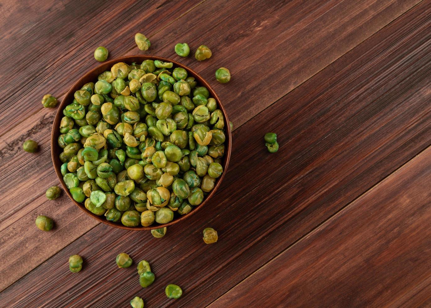 bovenaanzicht van gezouten groene erwten in houten kom op tafel, plat gelegd foto