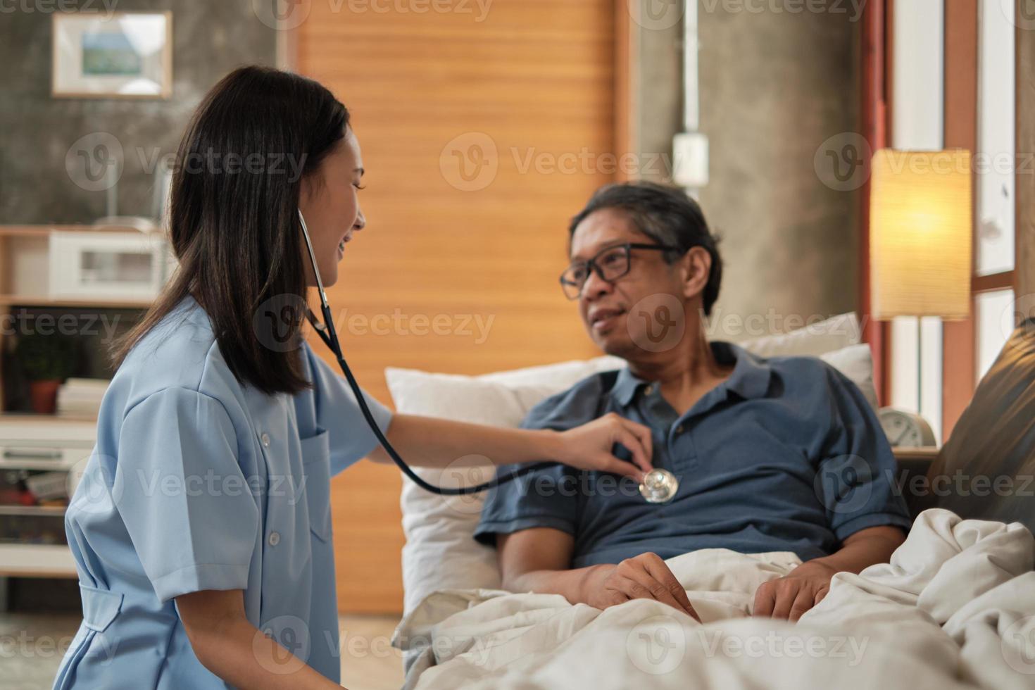 vrouwelijke arts die de gezondheid van Aziatische oudere mannelijke patiënt thuis controleert. foto