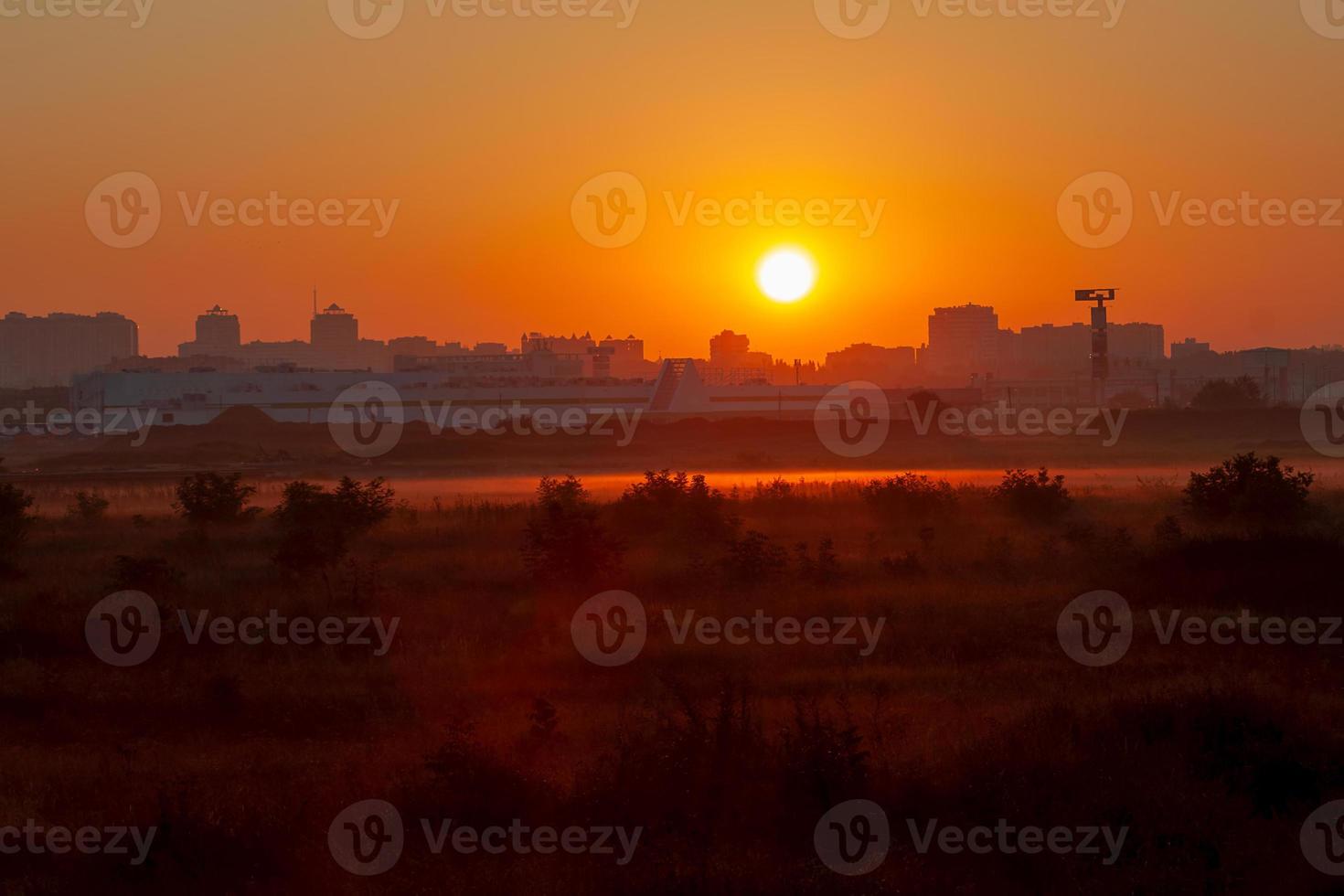 dageraad over de stad met contrastoranje lucht en mist in het veld foto