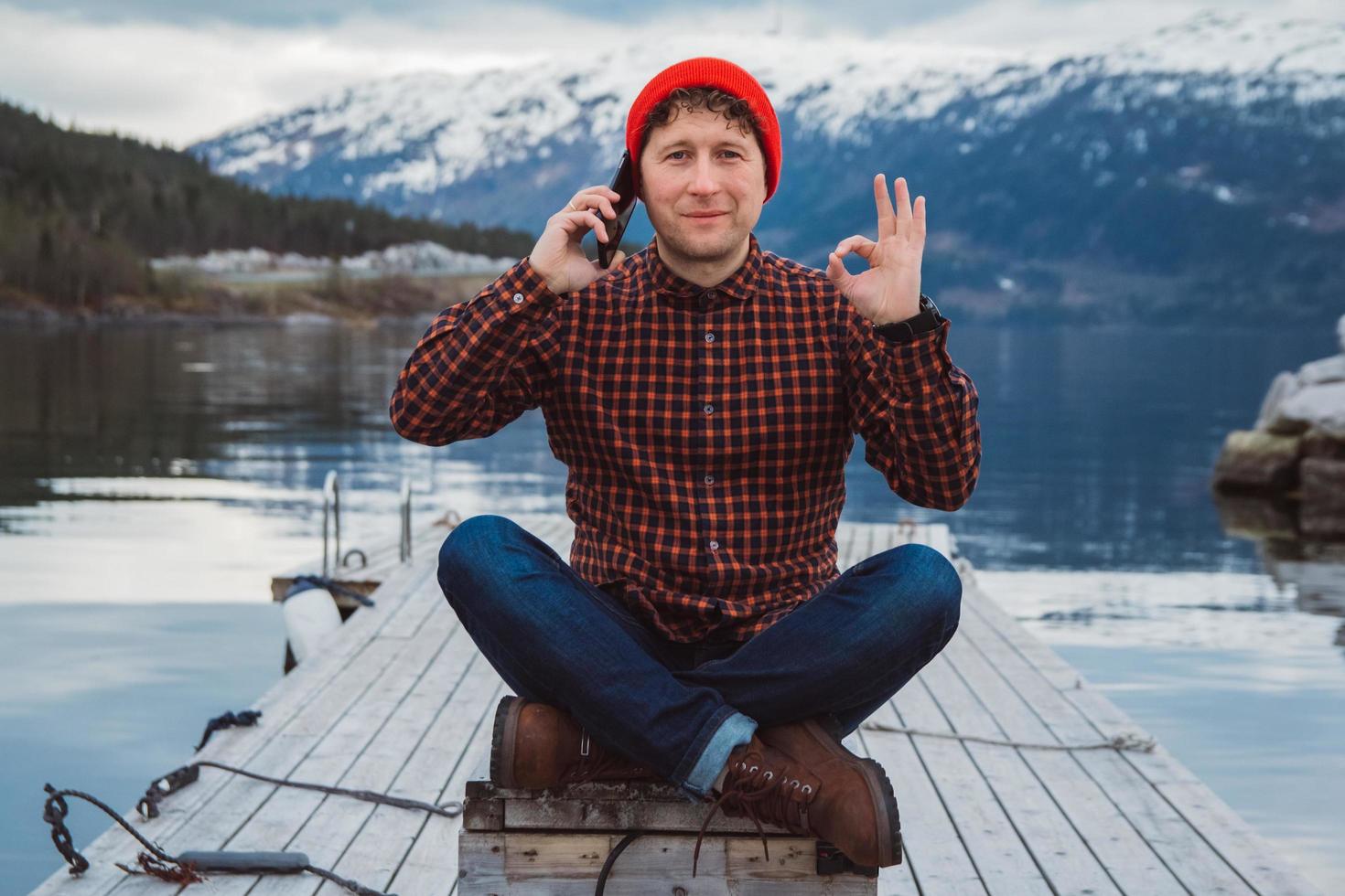 reiziger man praten op mobiele telefoon zittend op houten pier foto