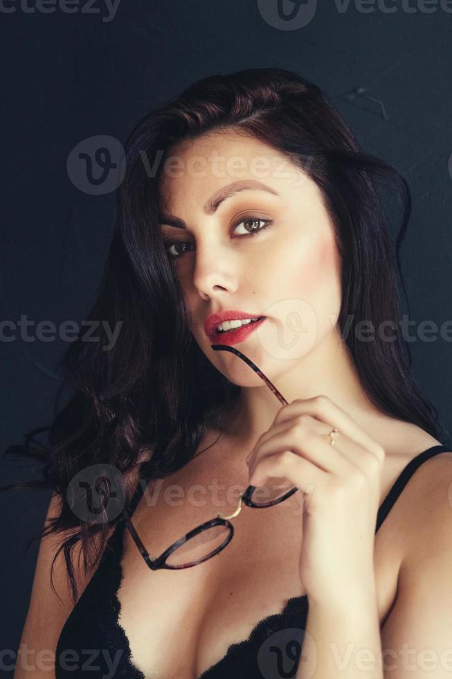mooie vrouw met een bril in de buurt van rode lippen op een zwarte achtergrond foto