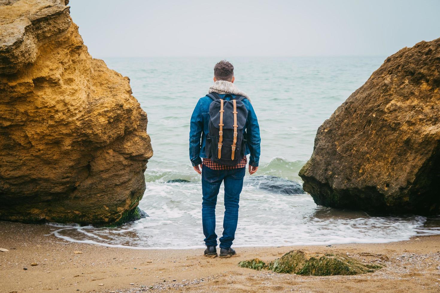 man met een rugzak die bij een rots staat tegen een prachtige zee foto