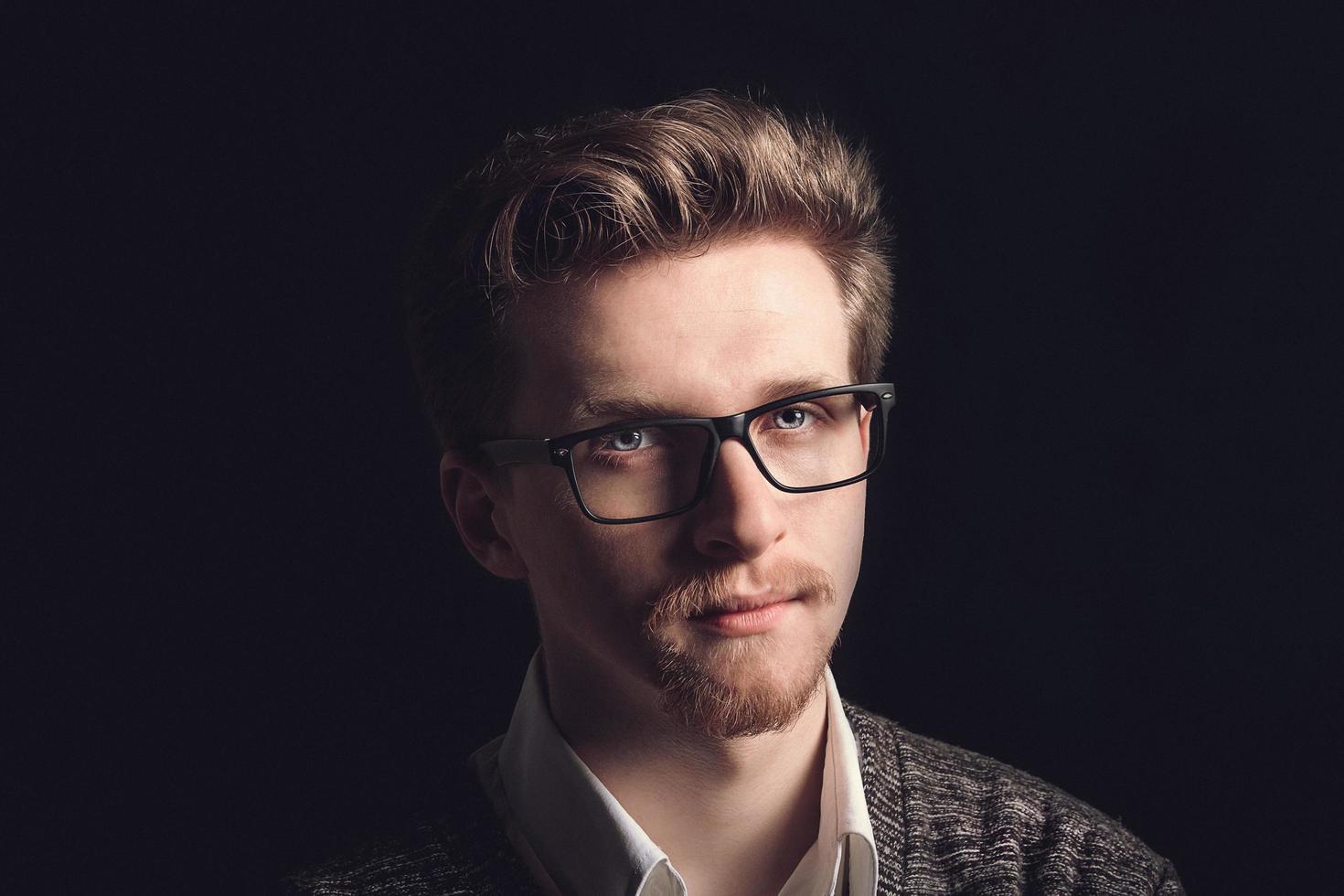 portret van een jonge man met een bril op een zwarte achtergrond foto