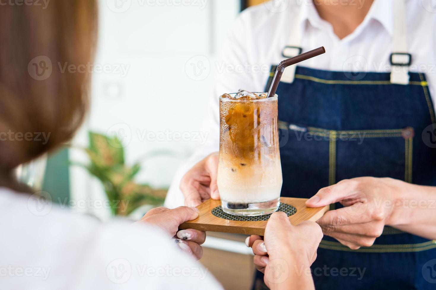 jonge barista bereidt iced latte om de klant in café te bedienen foto