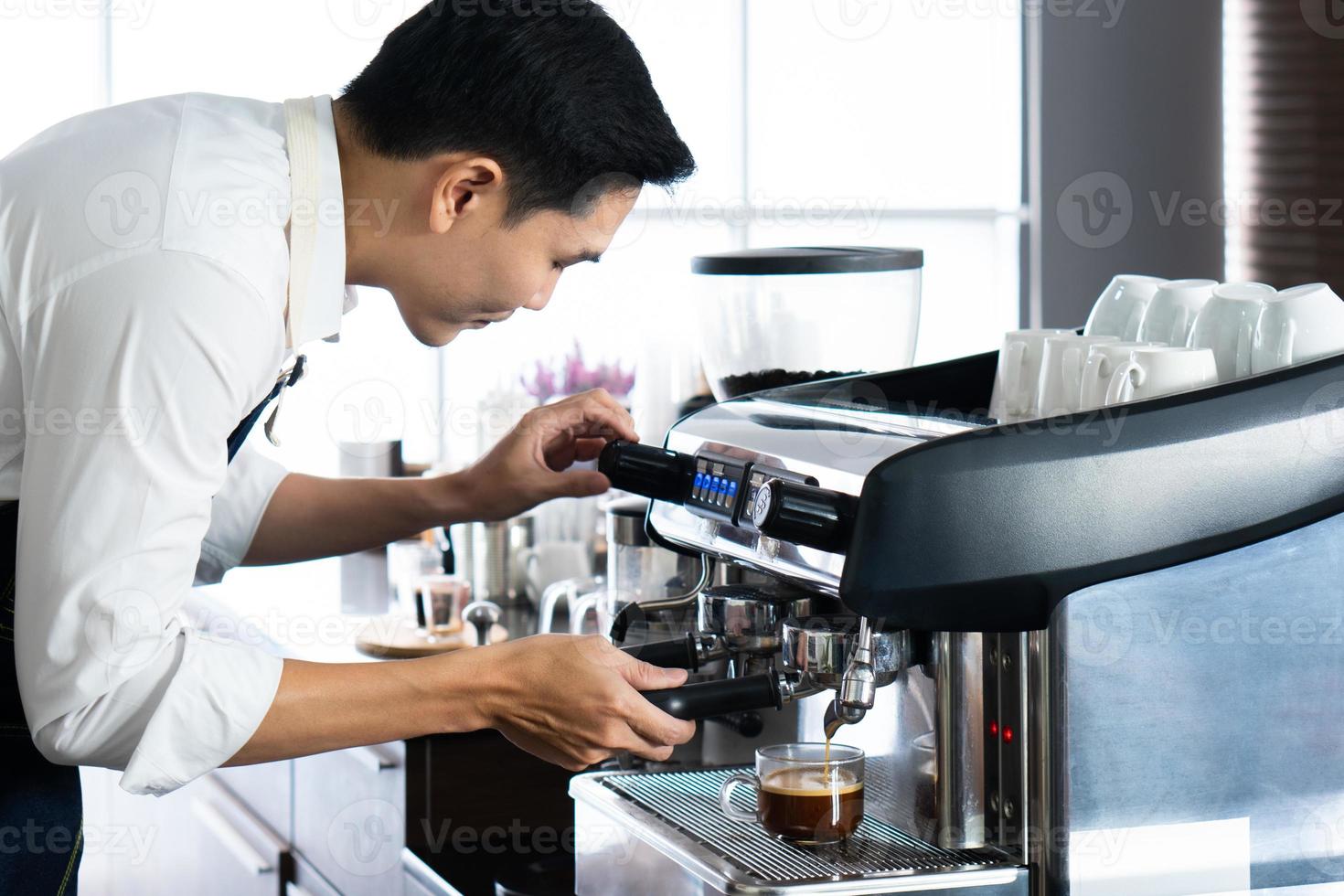 jonge Aziatische barista brouwt koffie uit een koffiezetapparaat in café foto