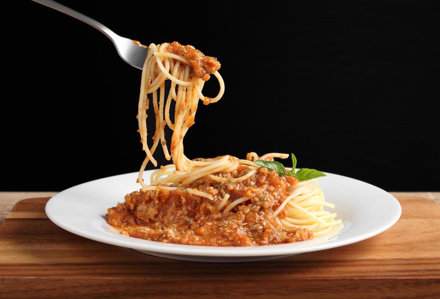 hand met een vork met spaghetti en rode saus in witte schotel foto