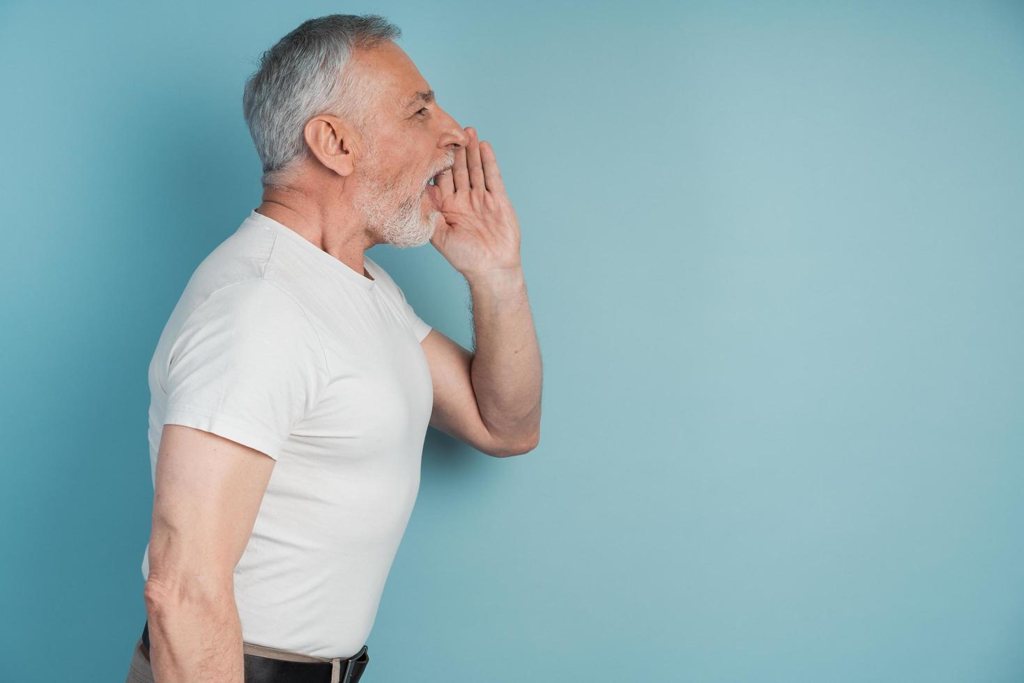 senior man met een grijze baard staat in profiel op een blauwe achtergrond foto