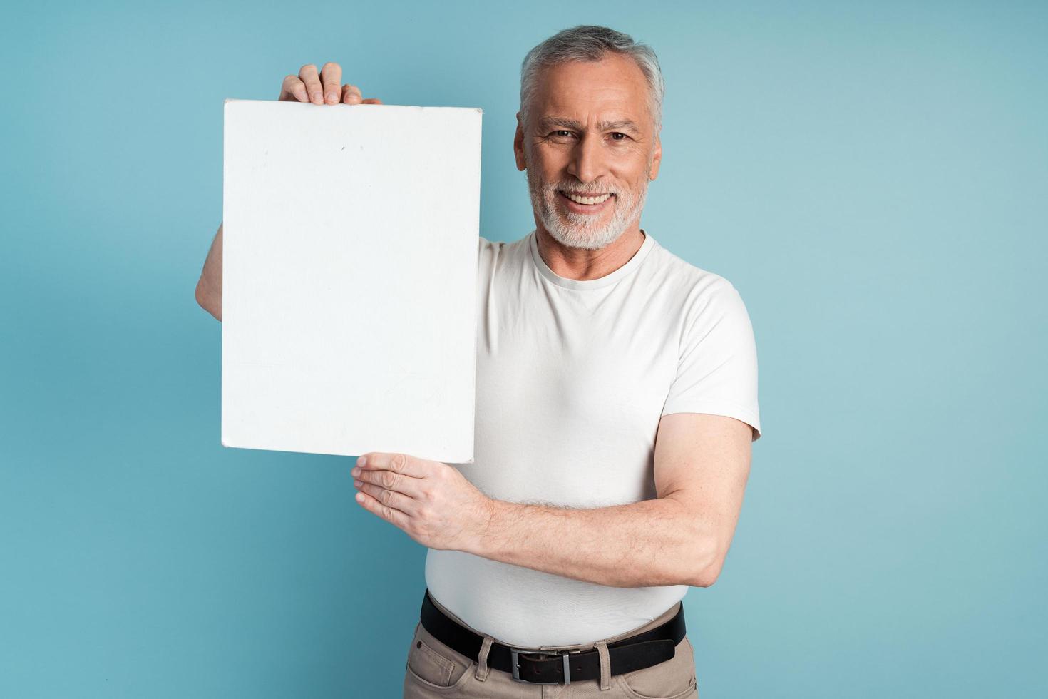 lachende gepensioneerde met een baard die een blanco vel papier vasthoudt foto