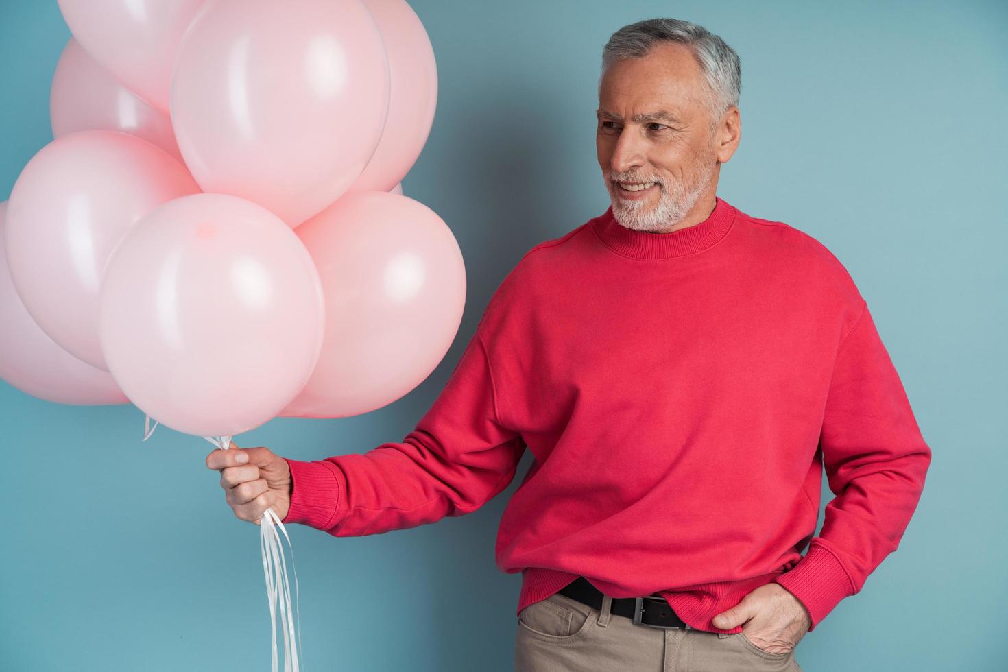 man met grijs haar en een baard houdt roze ballonnen vast foto