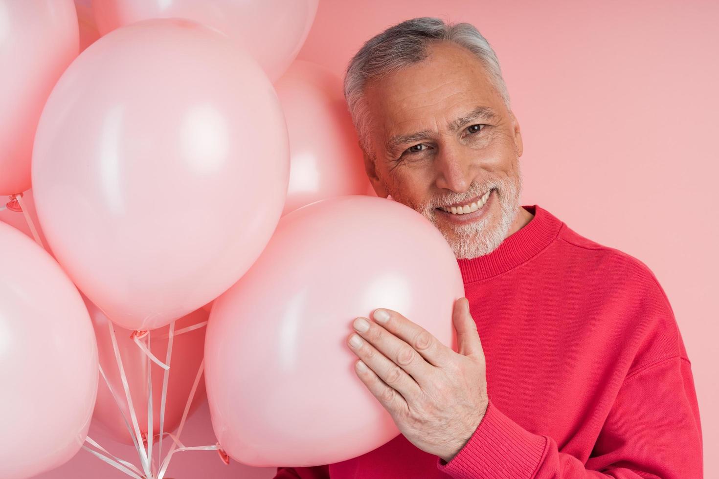 positieve, vrolijke man met ballonnen die zich voordeed op roze muurachtergrond foto