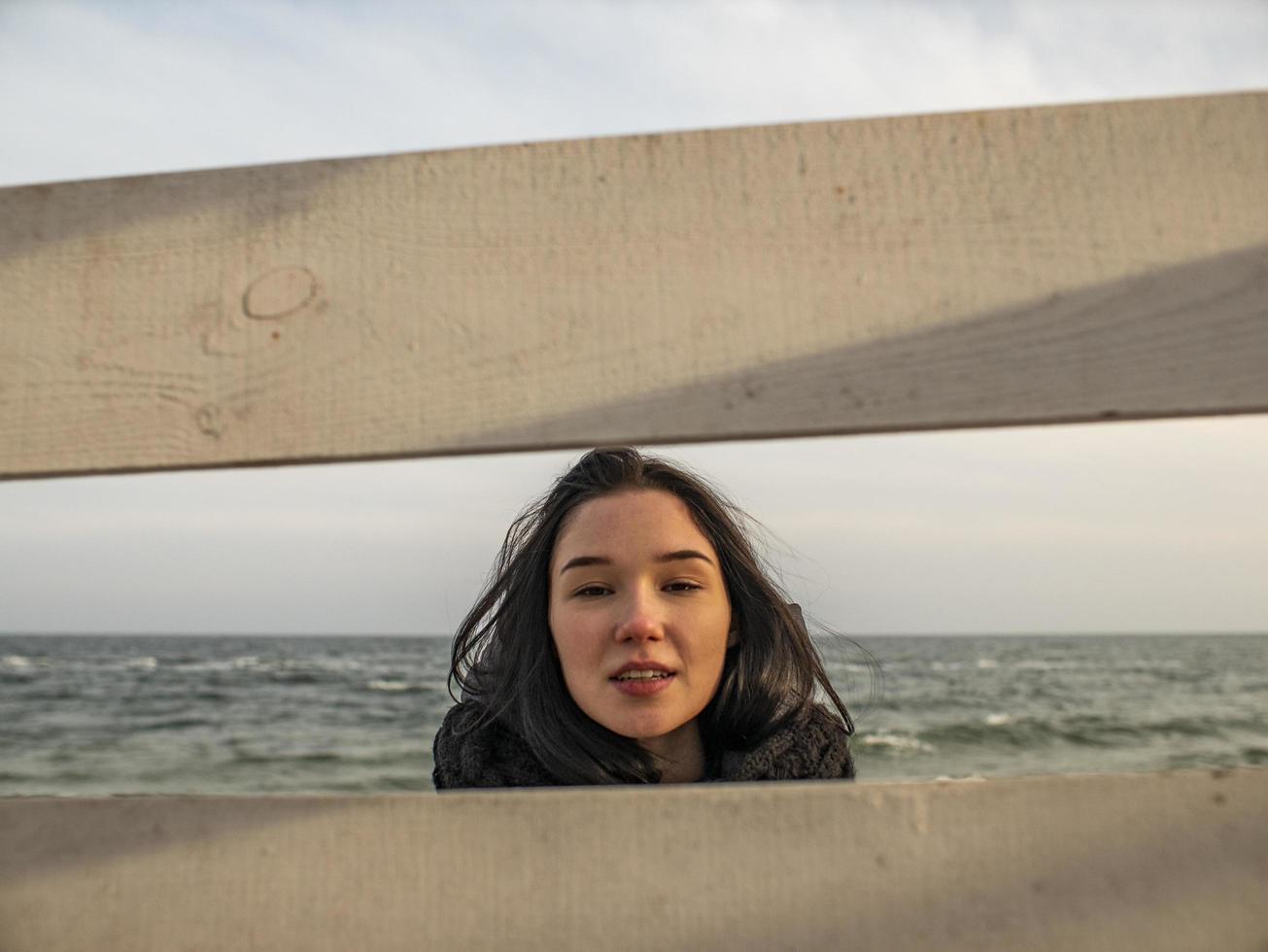 portret van een jong meisje met bruine haren, kijk door een houten hek foto