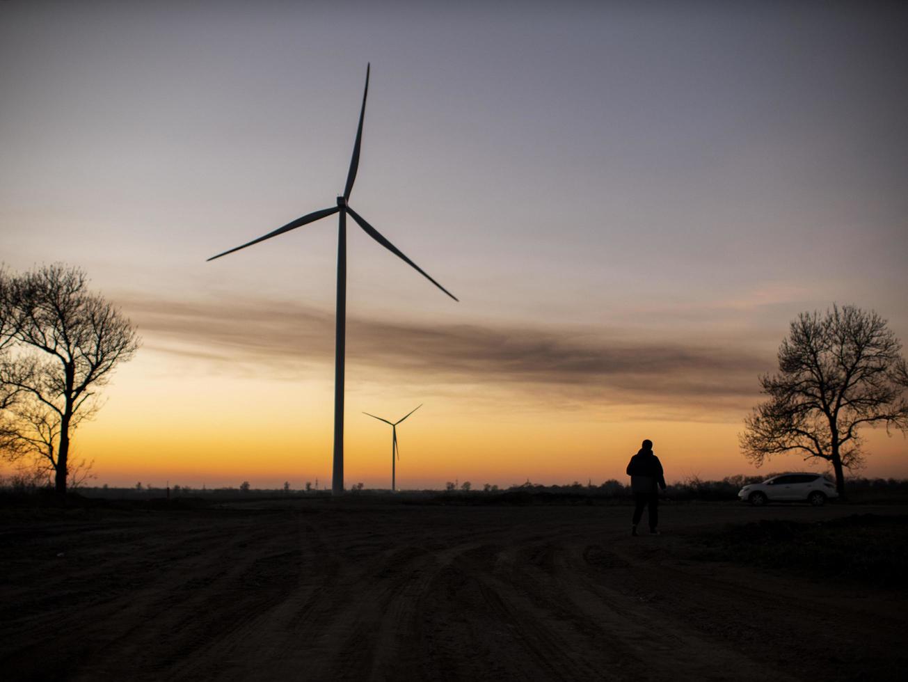 silhouet van een man gaat naar zonsondergang in de richting van windturbines foto