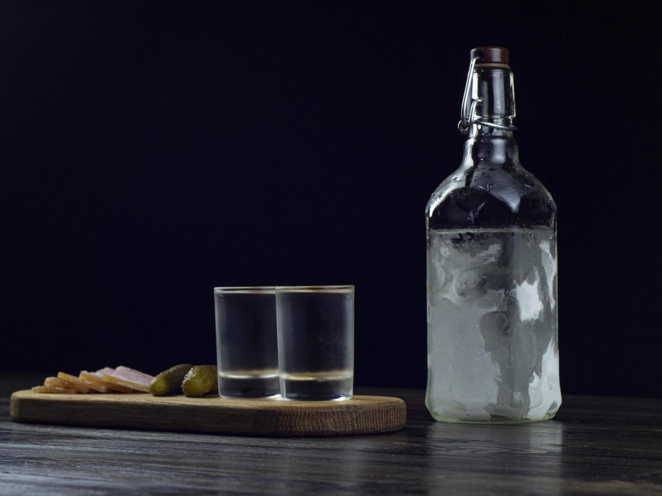 fles wodka, twee beslagen glazen met koude wodka op een houten plank foto