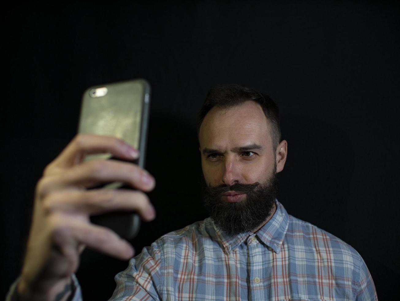 stijlvolle man met een baard en snor maakt selfie aan de telefoon foto