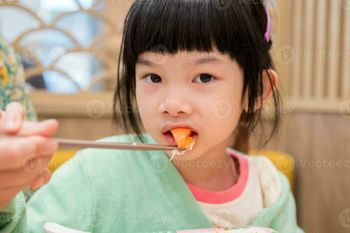 schattig weinig Aziatisch kind meisje aan het eten voedsel foto