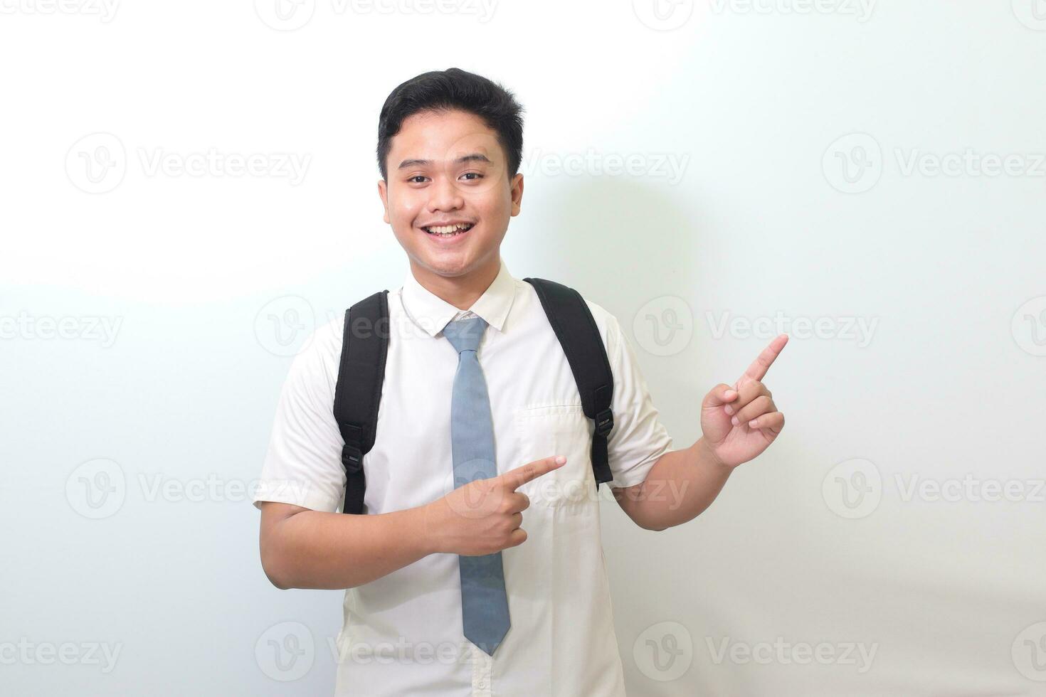 Indonesisch senior hoog school- leerling vervelend wit overhemd uniform met grijs stropdas tonen Product, richten Bij iets en lachend. geïsoleerd beeld Aan wit achtergrond foto