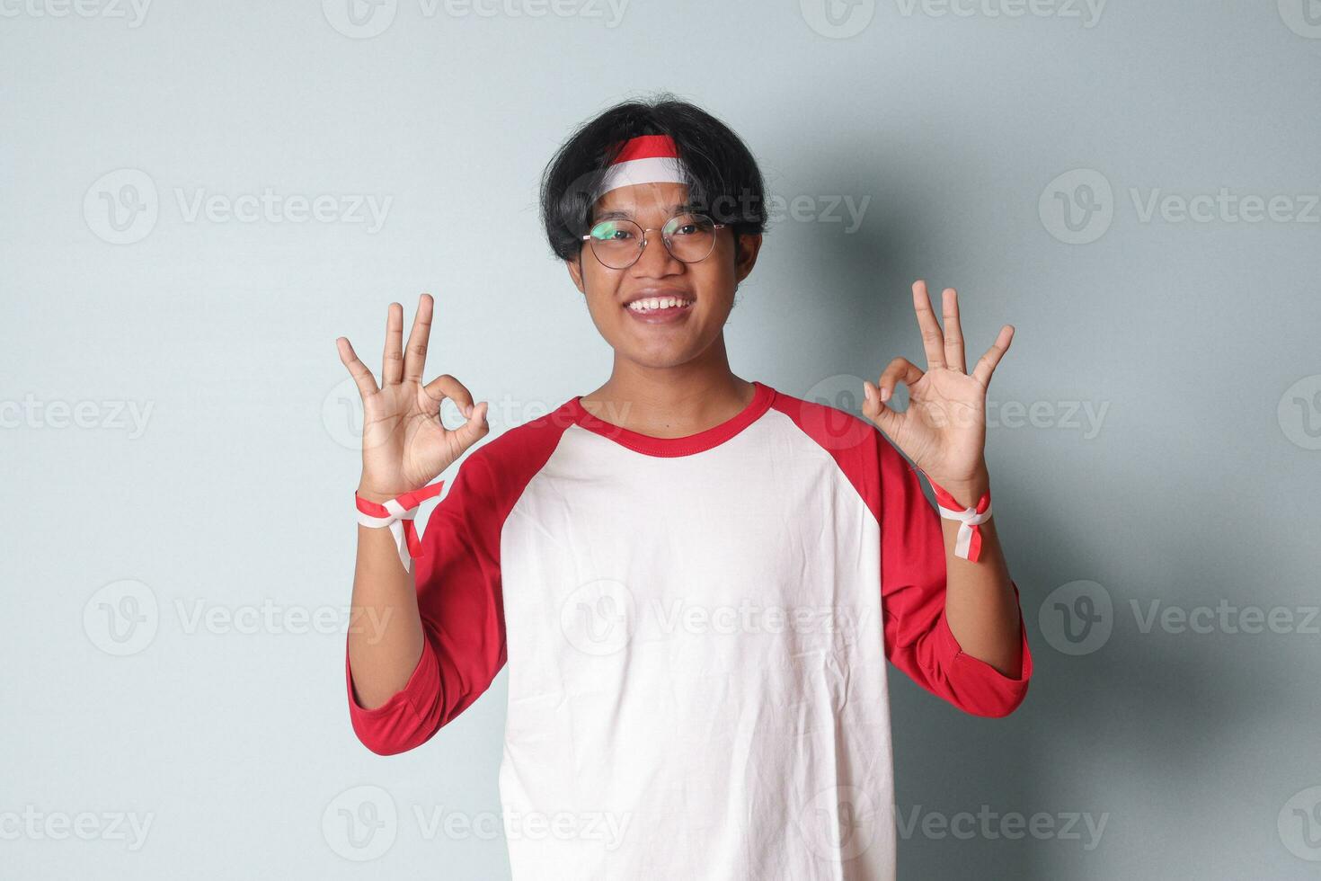 portret van aantrekkelijk Aziatisch Mens in t-shirt met rood en wit lint Aan hoofd, tonen OK hand- gebaar en lachend. geïsoleerd beeld Aan grijs achtergrond foto