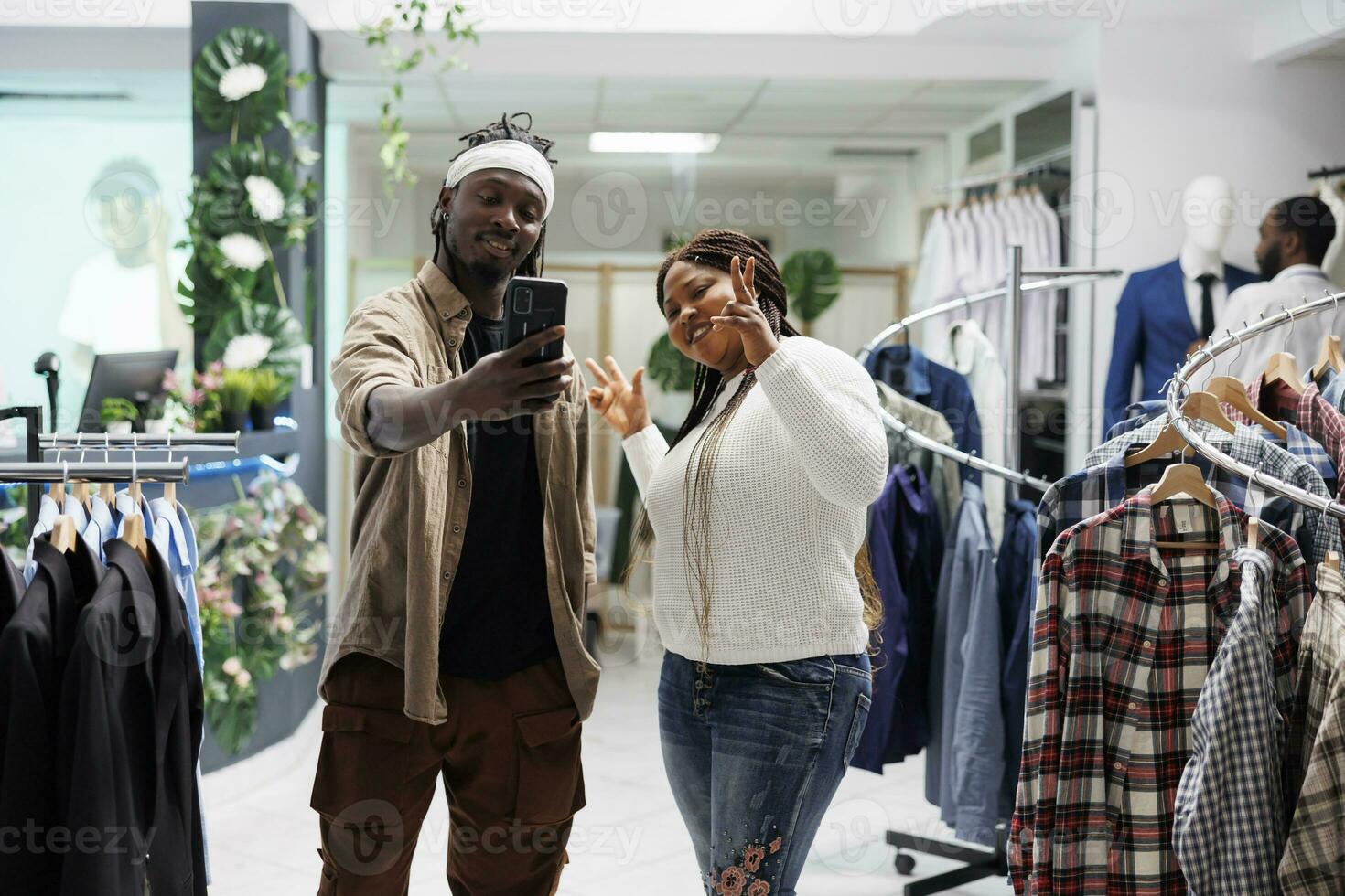 Afrikaanse Amerikaans Mens en vrouw beïnvloeders nemen selfie in mode boetiek. glimlachen sociaal media bloggers poseren voor mobiel telefoon foto terwijl bevorderen kleding merk in boodschappen doen winkelcentrum