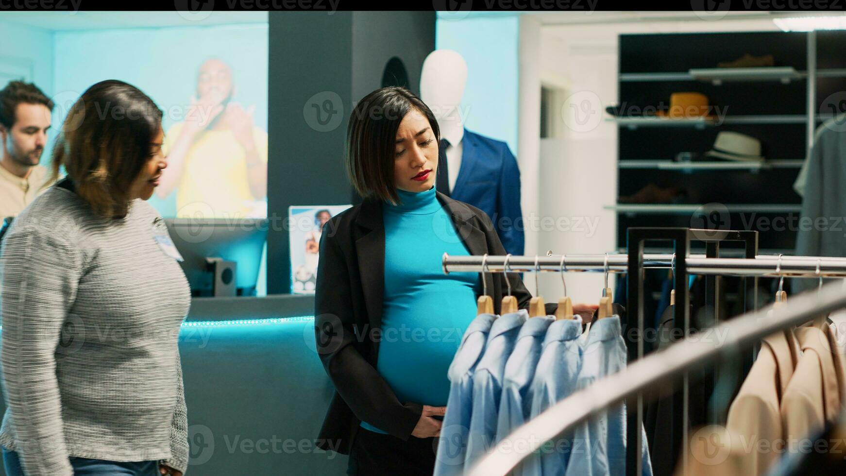 Aziatisch zwanger vrouw controle modern kleren Aan rekken, toekomst moeder op zoek naar kopen formeel dragen. jong cliënt met zwangerschap buik onderzoeken mode op te slaan handelswaar, baby buil. foto