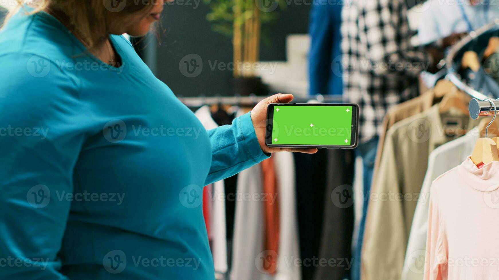 Afrikaanse Amerikaans vrouw analyseren telefoon met groene scherm sjabloon, op zoek Bij geïsoleerd Scherm in modern boetiek. elegant klant boodschappen doen voor modieus kleding in kleding op te slaan. mode concept foto