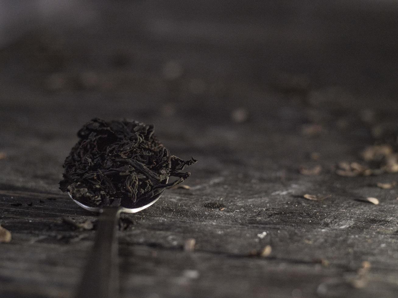 theelepel vol theeblad op een houten tafel. zwarte thee in een lepel. foto