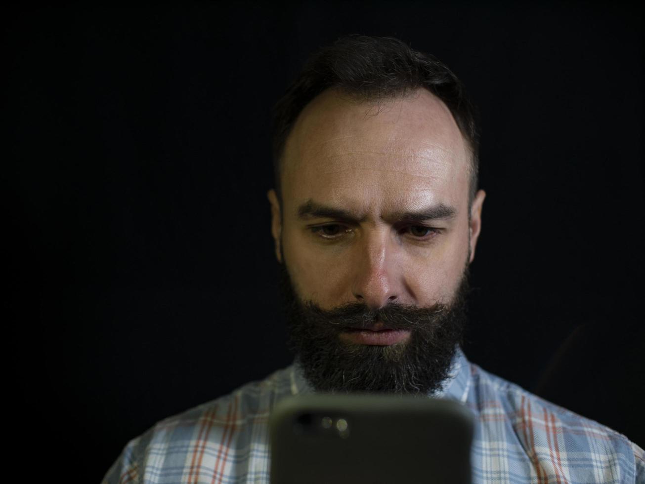 man met een baard en snor kijkt zorgvuldig naar de telefoon foto