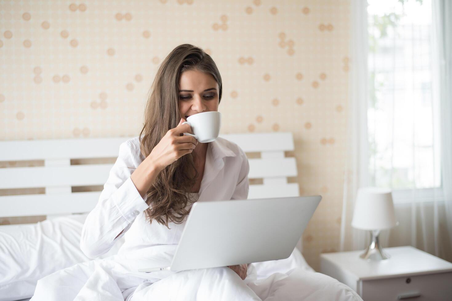 gelukkige mooie vrouw die aan laptop op het bed in het huis werkt foto