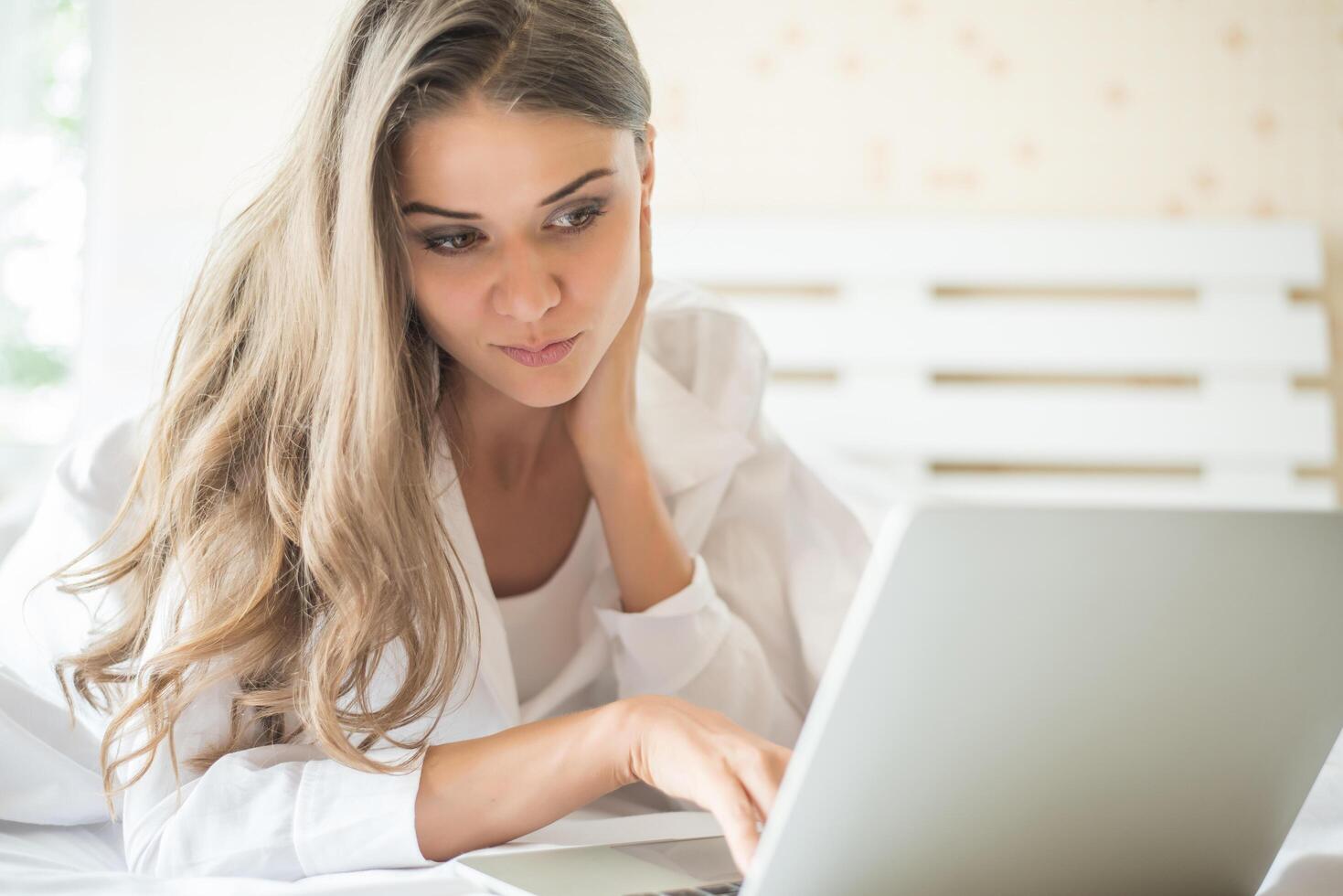 gelukkige mooie vrouw die aan laptop op het bed in het huis werkt foto