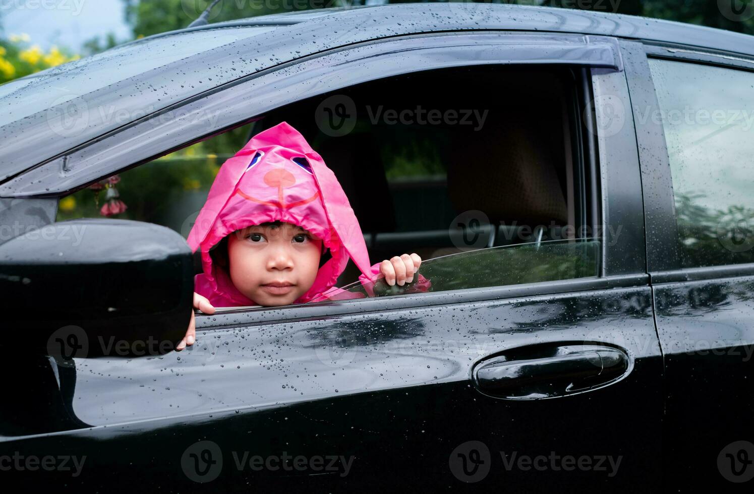 Aziatisch meisje vervelend een roze regenjas in de auto. wachtte voor zijn ouders naar plukken hem omhoog terwijl school- was over. foto