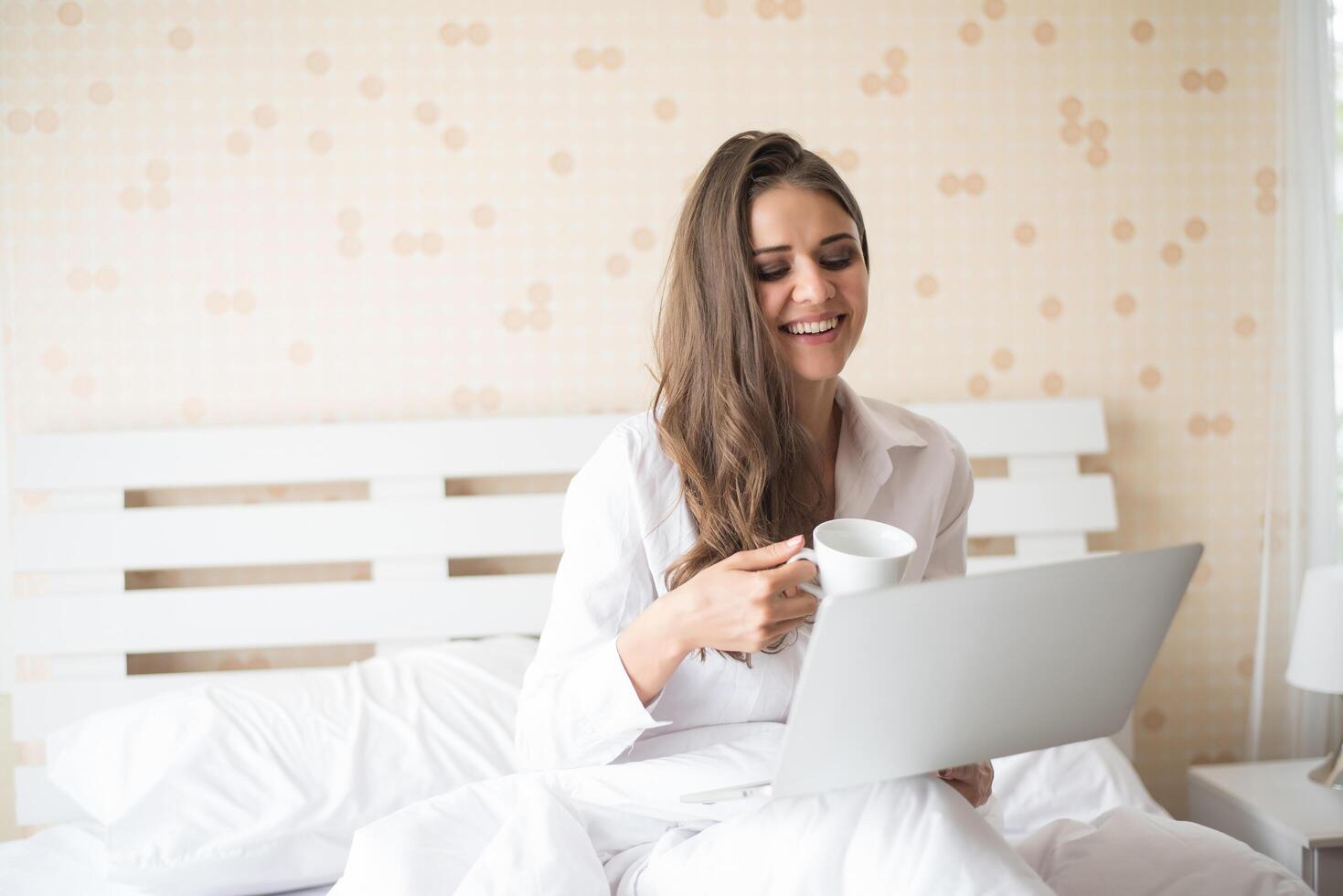 gelukkige mooie vrouw die aan laptop op het bed in het huis werkt foto