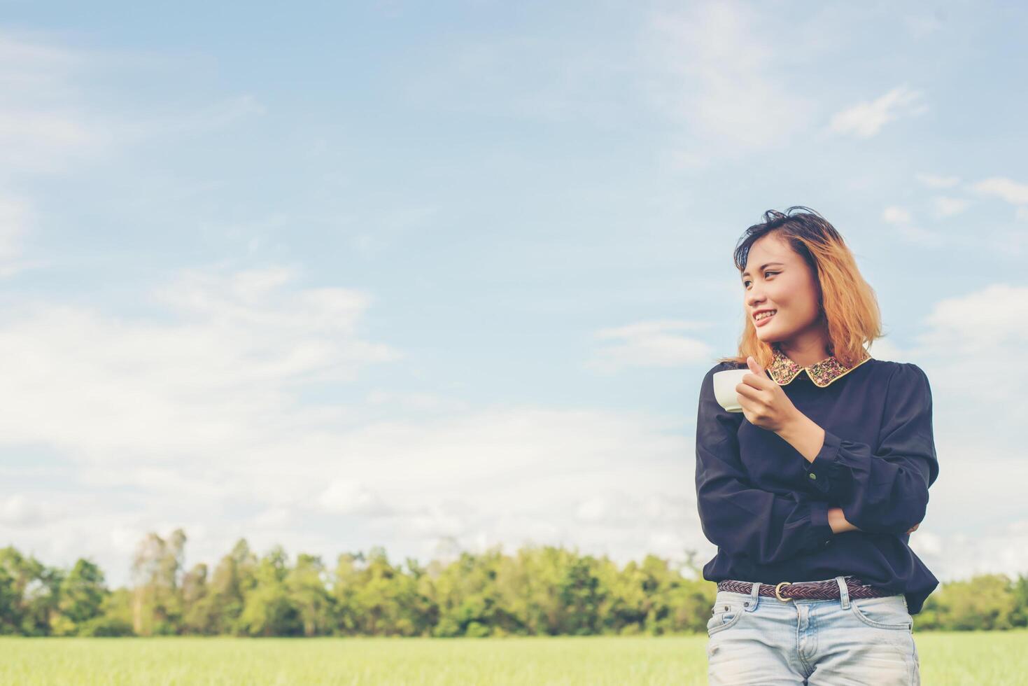 achterkant van gelukkige jonge vrouw die op het groene veld staat, geniet met frisse lucht foto