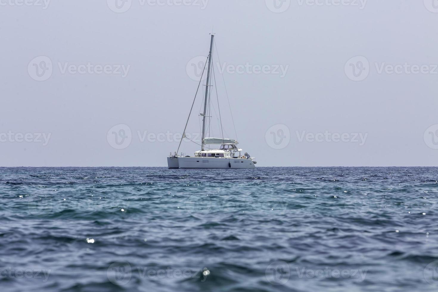 witte zeilboot catamaran op oceaan in de buurt van strand. foto