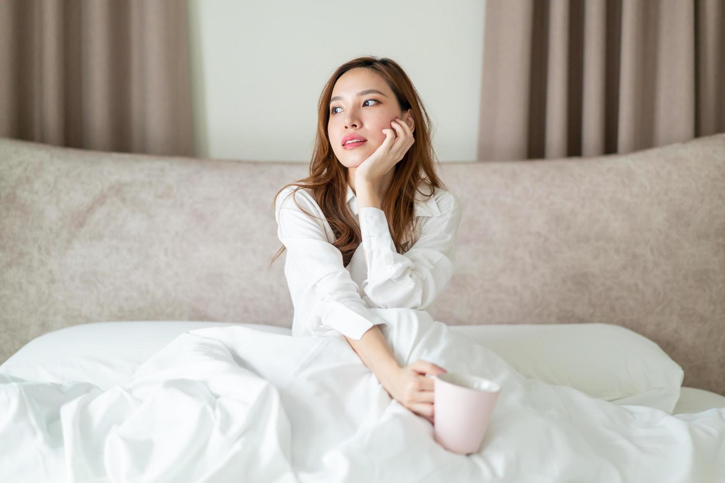 portret mooie aziatische vrouw wordt wakker en houdt 's ochtends een koffiekopje of mok op bed foto