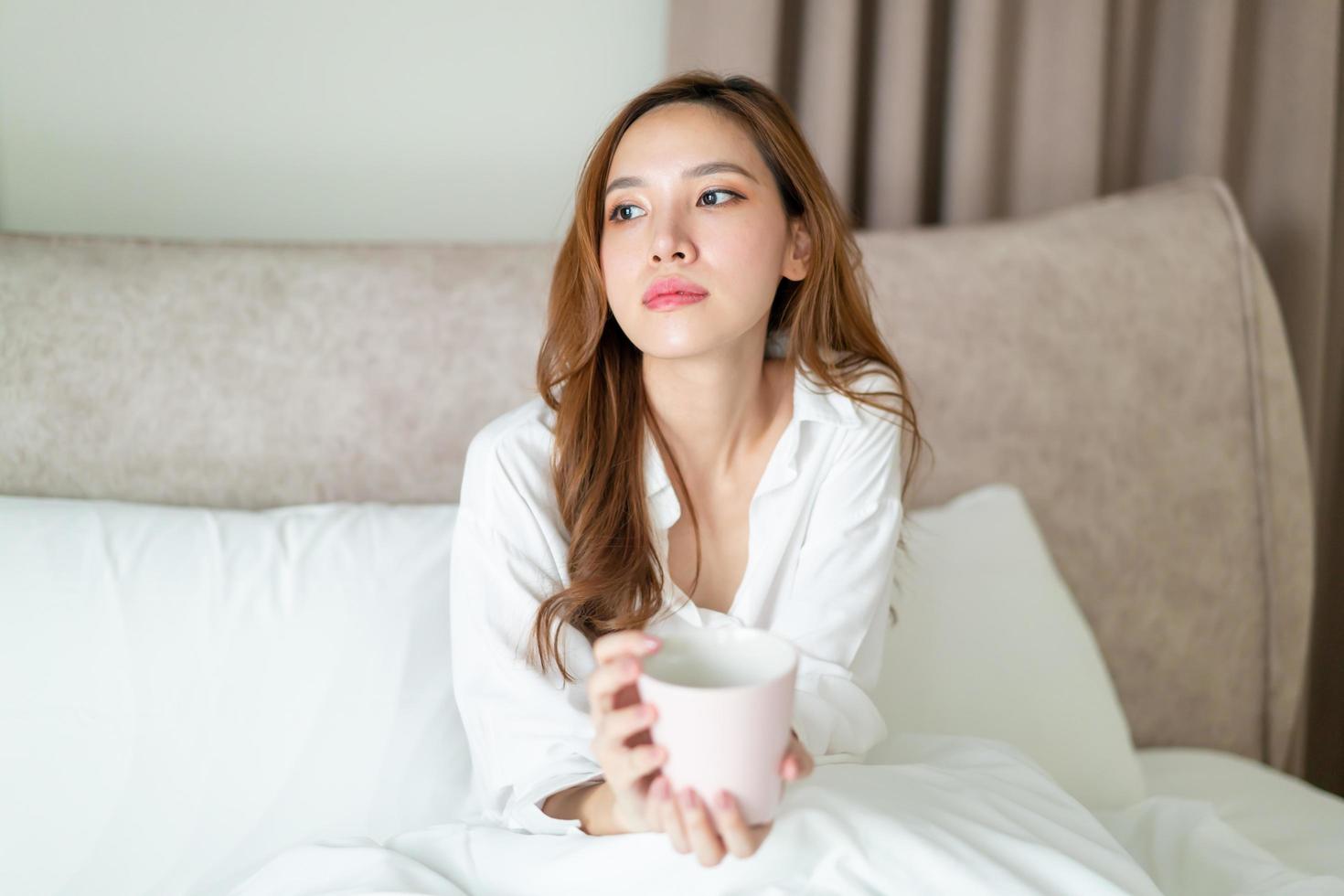 portret mooie aziatische vrouw wordt wakker en houdt 's ochtends een koffiekopje of mok op bed foto